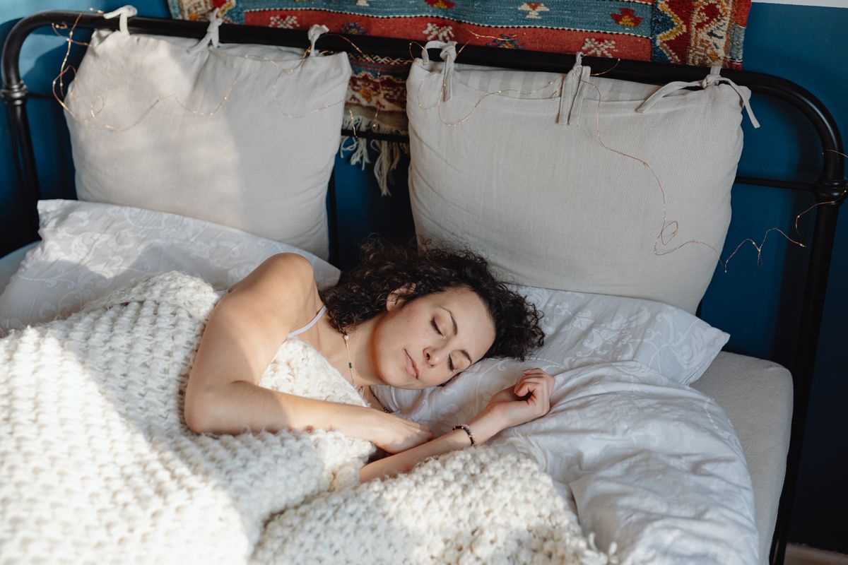 Mulher dormindo tranquila em uma cama com mantas de tricô, sob a luz da manhã
